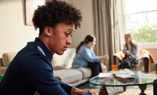 A young man sitting separately from friends and family, looking troubled