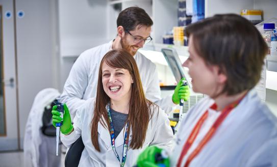 A group of researchers in white lab coats interacting with lab equipment