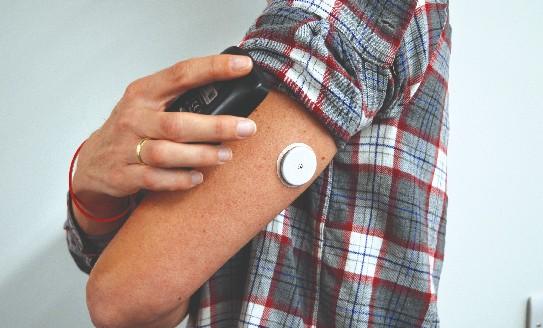 a close up photo of a Flash monitor (A small white circle) on a man's upper arm, which he is scanning with a reader device