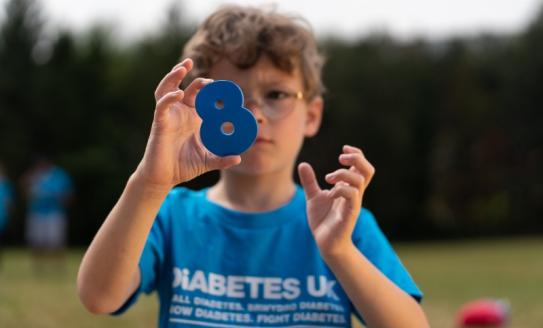 The image shows a young boy in a blue t-shirt holding the number 8.