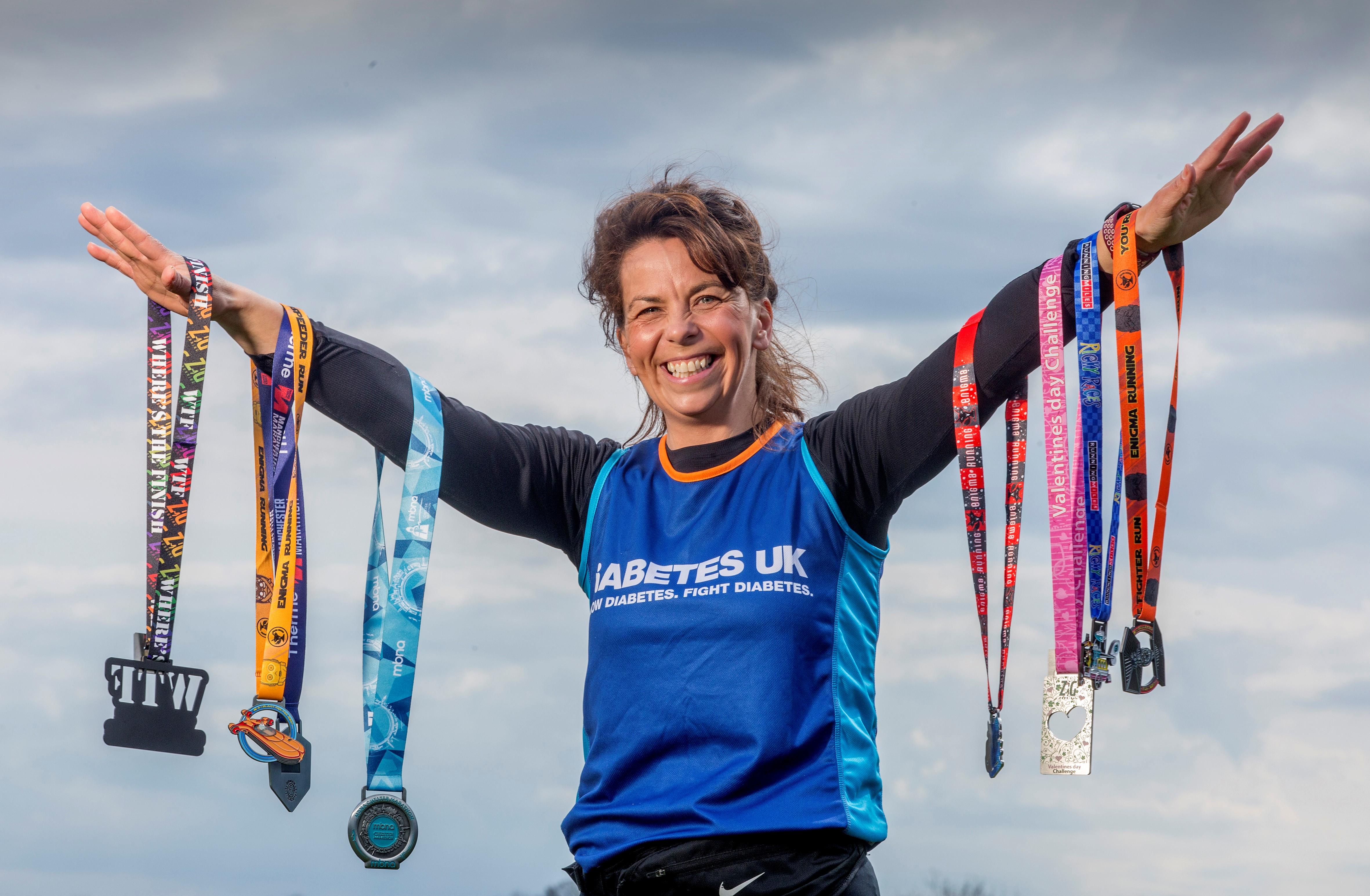 Lucy holds 7 medals up. She is smiling and wearing her Diabetes UK Vest.