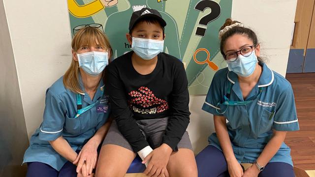 A photo of Mahn sitting in a hospital ward between two of the research nurses, all wearing masks