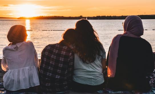 Four children face away from the camera and look towards a sunset