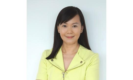 Professor Ng smiling towards camera in front of a white wall, wearing a yellow jacket