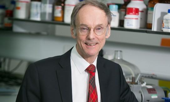 Professor Taylor wearing a suit and smiling towards camera with a lab bench and shelves visible behind him