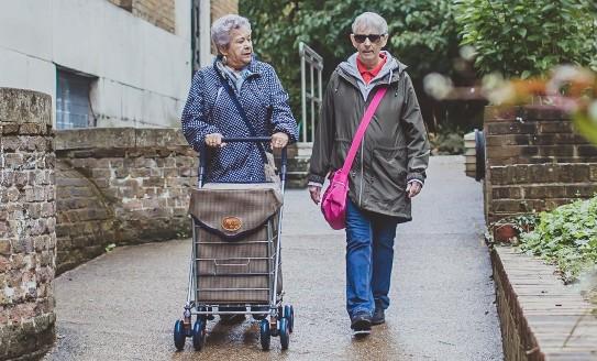 Two older ladies walking together, one pushing a shopping trolley 